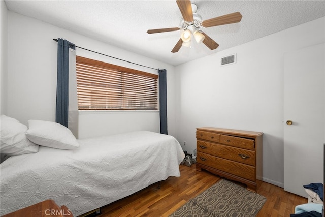 bedroom featuring a textured ceiling, wood finished floors, visible vents, and a ceiling fan