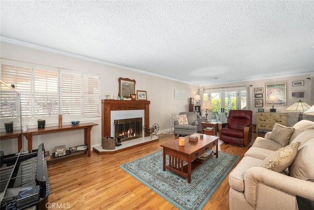 living area with a textured ceiling, baseboards, light wood-style floors, ornamental molding, and a glass covered fireplace