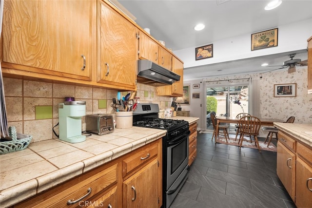 kitchen featuring ceiling fan, under cabinet range hood, stainless steel gas range, tile counters, and wallpapered walls