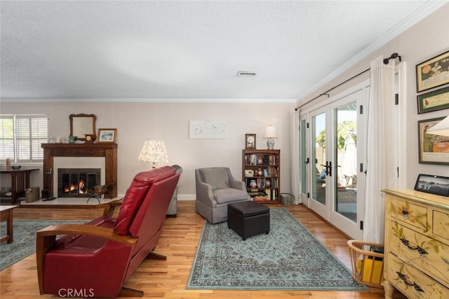 living room featuring crown molding, a glass covered fireplace, visible vents, and a healthy amount of sunlight