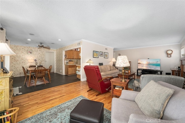 living room featuring ceiling fan, a textured ceiling, wood finished floors, wallpapered walls, and crown molding