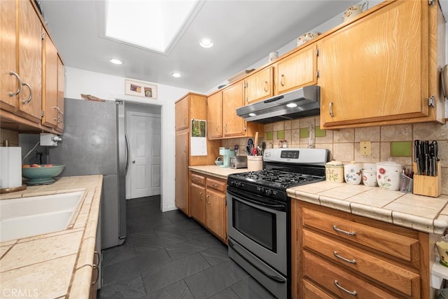 kitchen featuring stainless steel appliances, a skylight, under cabinet range hood, and decorative backsplash