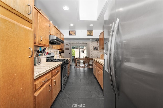 kitchen featuring tile countertops, recessed lighting, decorative backsplash, appliances with stainless steel finishes, and under cabinet range hood