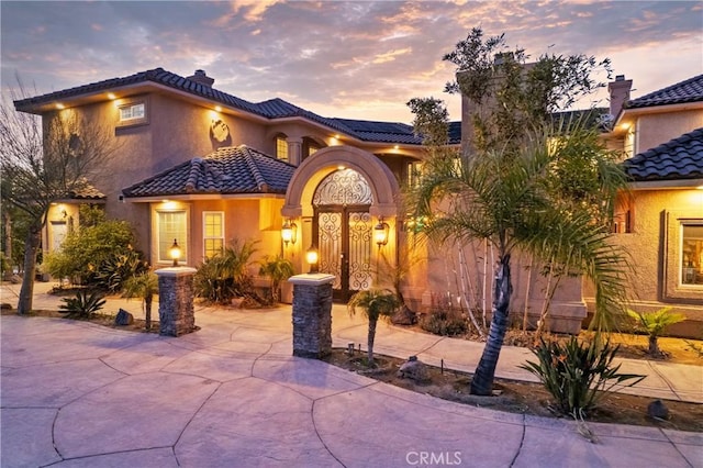 mediterranean / spanish-style home with a tiled roof, roof mounted solar panels, and stucco siding