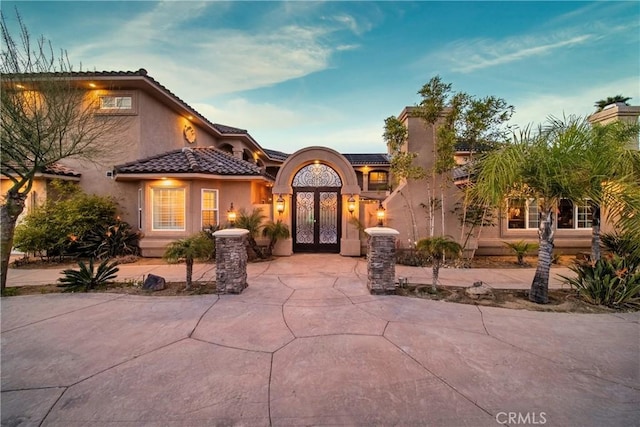 mediterranean / spanish-style home featuring french doors, a tile roof, and stucco siding