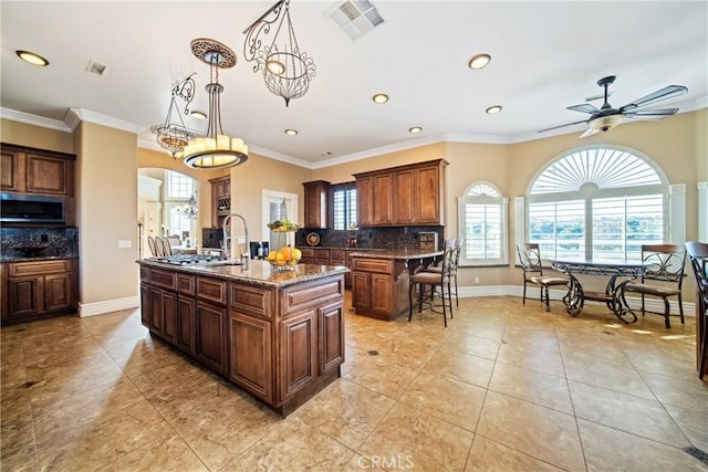 kitchen with stainless steel microwave, backsplash, ornamental molding, and a kitchen island with sink