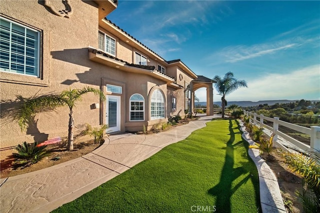 exterior space with stucco siding, a tiled roof, a lawn, and fence