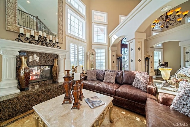 living room featuring arched walkways, a healthy amount of sunlight, a high end fireplace, and ornate columns