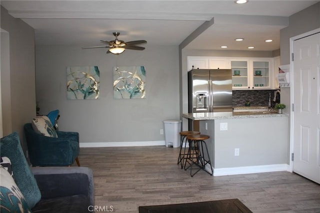 kitchen featuring a peninsula, white cabinetry, stainless steel refrigerator with ice dispenser, light stone countertops, and glass insert cabinets