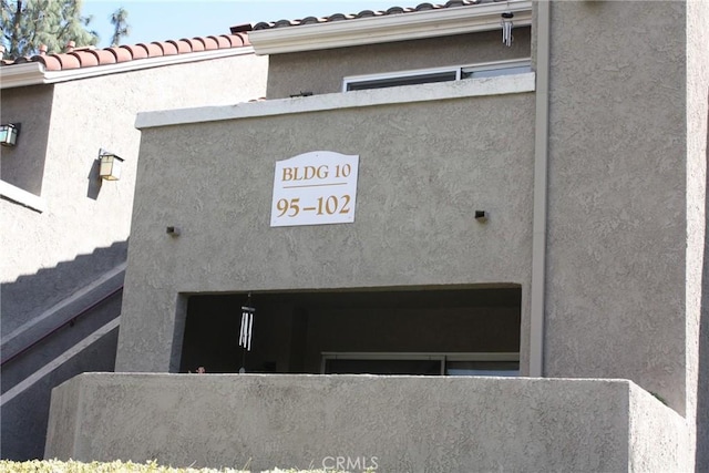 details featuring a downspout, a tiled roof, and stucco siding