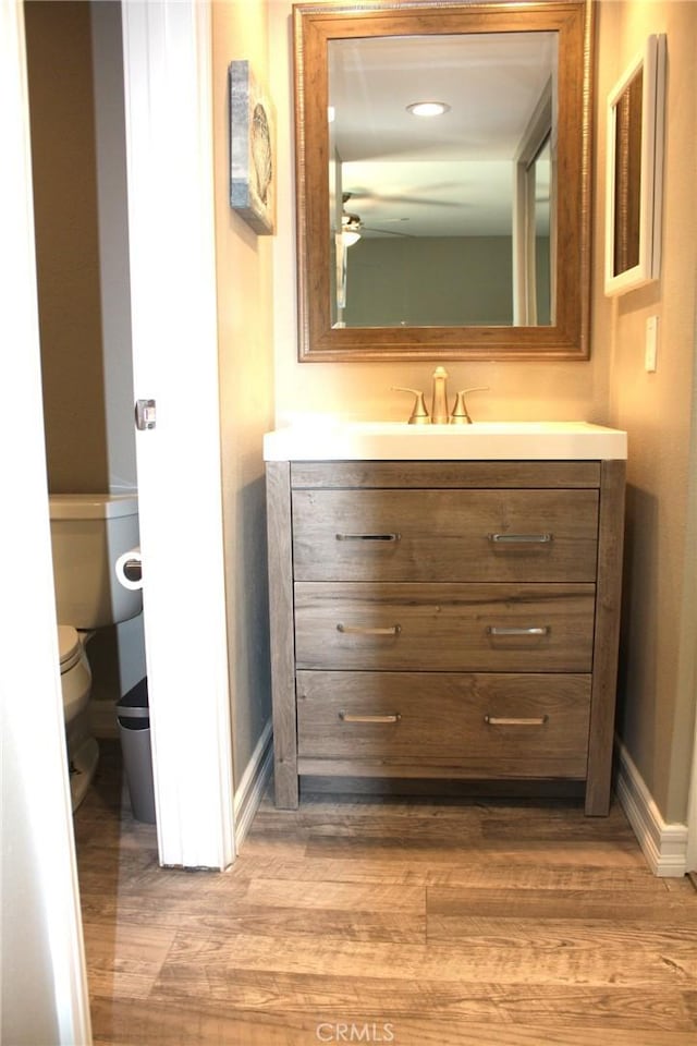 bathroom with baseboards, vanity, toilet, and wood finished floors