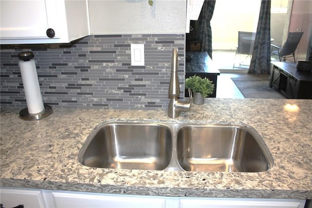 interior details with white cabinets, a sink, backsplash, and light stone countertops