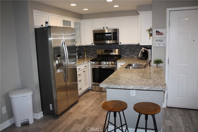 kitchen featuring wood finished floors, appliances with stainless steel finishes, a sink, and white cabinets