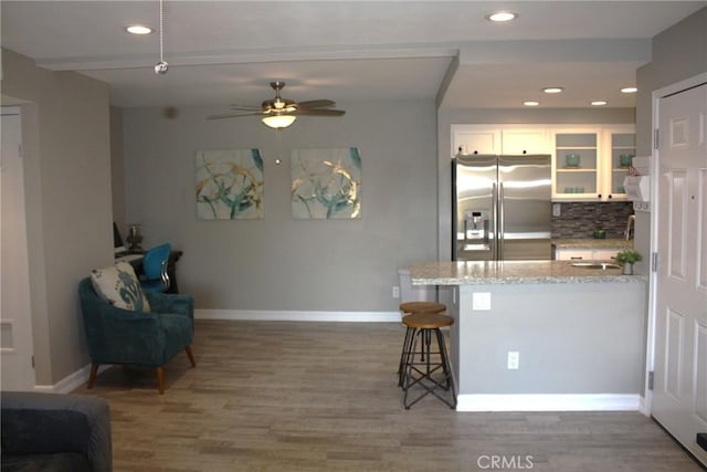 kitchen with stainless steel fridge, light stone counters, a sink, white cabinetry, and backsplash