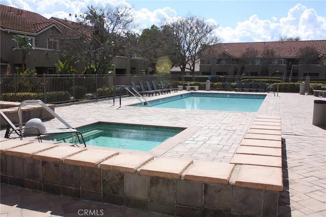 community pool with a patio area, a hot tub, and fence