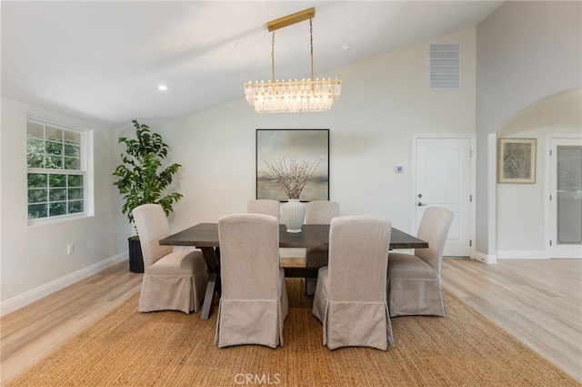 dining space with visible vents, baseboards, vaulted ceiling, light wood-style floors, and arched walkways