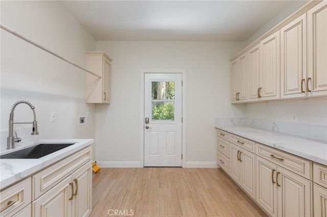 laundry area with cabinet space, light wood-style flooring, baseboards, and a sink