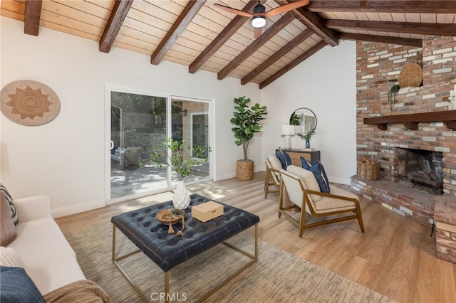 living area with ceiling fan, a brick fireplace, light wood-style flooring, and beam ceiling