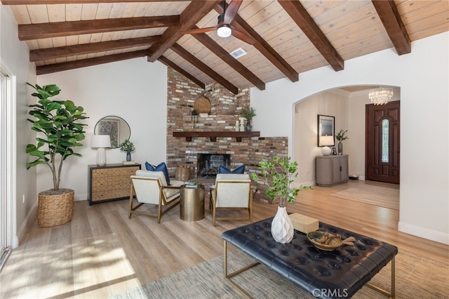 living area featuring beam ceiling, a fireplace, wooden ceiling, wood finished floors, and arched walkways