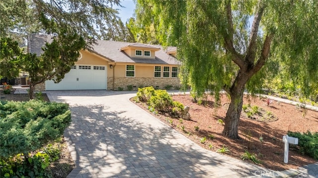 ranch-style home with a tiled roof, stucco siding, decorative driveway, stone siding, and an attached garage