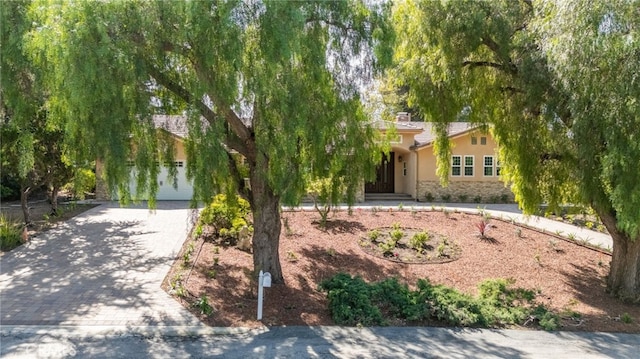 obstructed view of property with decorative driveway, stone siding, and stucco siding