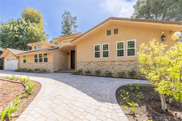 view of front of home featuring a tiled roof, stucco siding, driveway, stone siding, and an attached garage