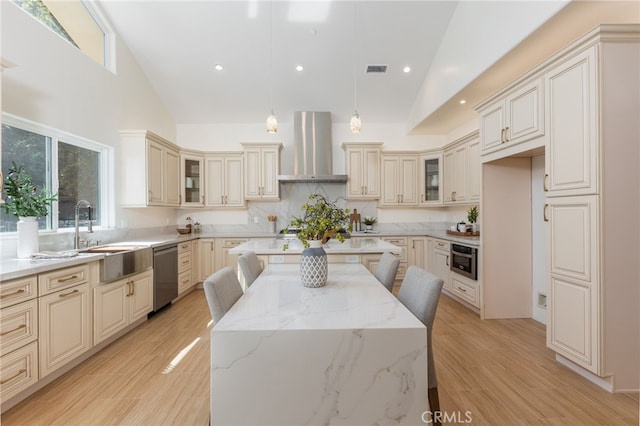 kitchen featuring stainless steel appliances, cream cabinets, a center island, and wall chimney range hood