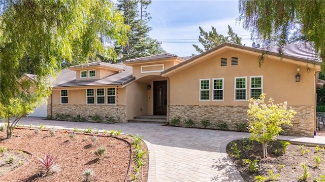 view of front of home featuring a tiled roof, stone siding, driveway, and stucco siding