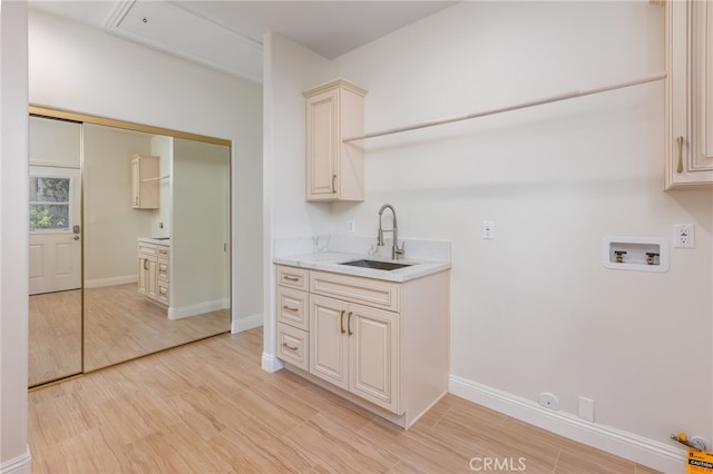 laundry area with baseboards, cabinet space, a sink, washer hookup, and light wood-style floors