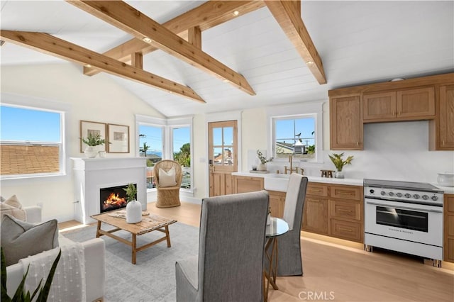 interior space featuring vaulted ceiling with beams, a lit fireplace, and light wood finished floors