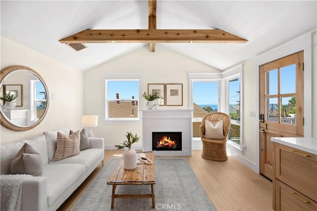 living room with vaulted ceiling with beams, a warm lit fireplace, wood finished floors, visible vents, and baseboards