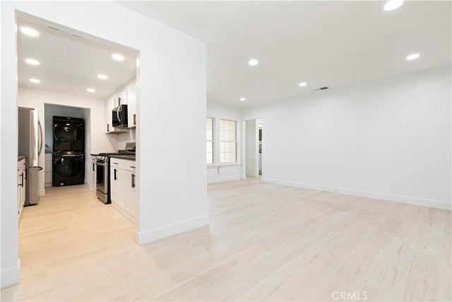 interior space featuring recessed lighting, white cabinetry, light wood-style floors, appliances with stainless steel finishes, and stacked washer and clothes dryer