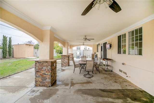 view of patio featuring a ceiling fan, outdoor dining area, an outdoor structure, and a storage unit