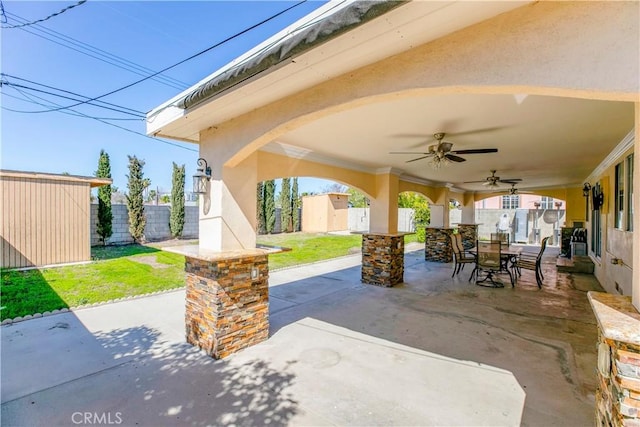 view of patio featuring outdoor dining space, ceiling fan, fence, a shed, and an outdoor structure