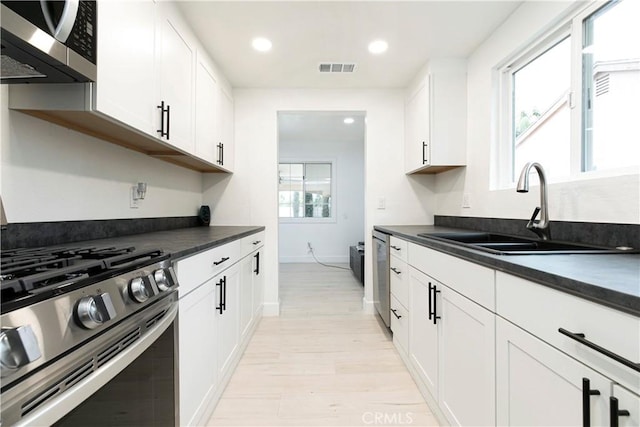 kitchen with stainless steel appliances, dark countertops, light wood-style floors, white cabinetry, and a sink