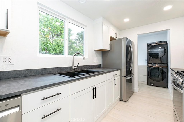 kitchen with dark countertops, appliances with stainless steel finishes, stacked washer / dryer, white cabinetry, and a sink