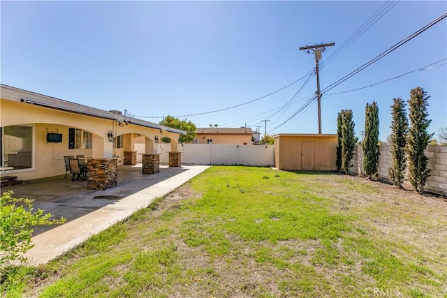 view of yard featuring a patio area, a fenced backyard, a storage unit, and an outbuilding