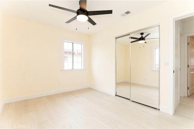 unfurnished bedroom with a closet, visible vents, ceiling fan, wood finished floors, and baseboards