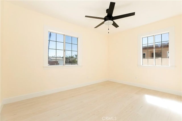 empty room with a ceiling fan, plenty of natural light, baseboards, and wood finished floors