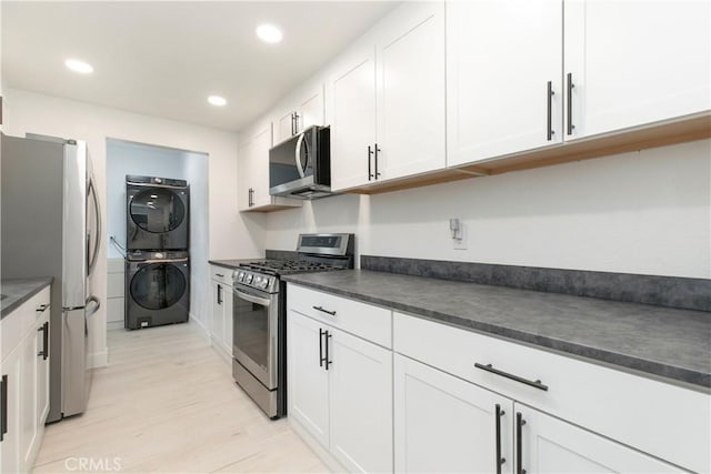 kitchen featuring dark countertops, white cabinetry, stainless steel appliances, and stacked washer / drying machine