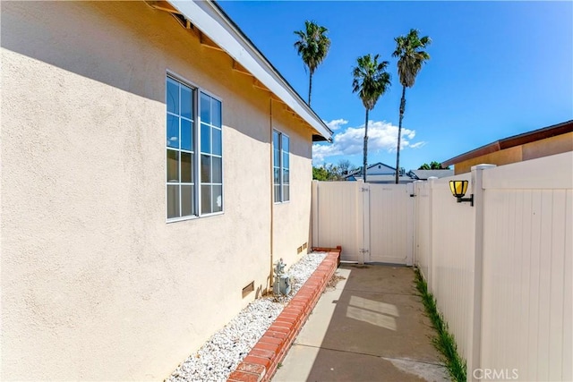 view of home's exterior featuring a gate, fence, crawl space, and stucco siding