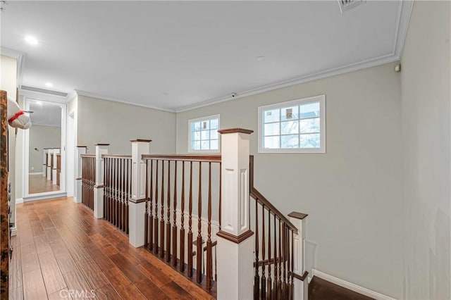 hallway featuring baseboards, visible vents, ornamental molding, wood finished floors, and an upstairs landing