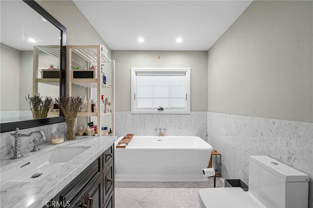 bathroom with wainscoting, toilet, a freestanding bath, vanity, and recessed lighting