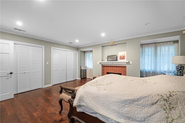 bedroom with visible vents, wood finished floors, crown molding, a brick fireplace, and multiple closets