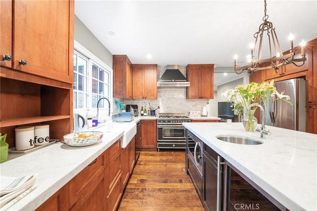 kitchen featuring dark wood-style flooring, appliances with stainless steel finishes, brown cabinetry, a sink, and wall chimney exhaust hood