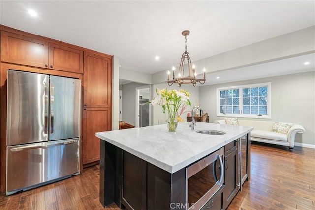 kitchen with brown cabinets, dark wood finished floors, stainless steel appliances, a sink, and light stone countertops