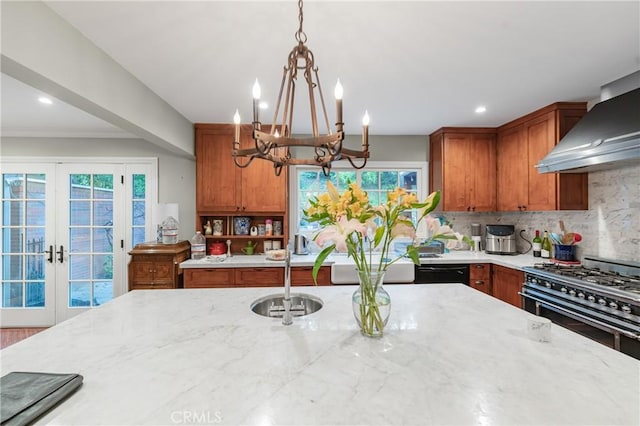 kitchen featuring light stone counters, brown cabinets, wall chimney range hood, double oven range, and a sink