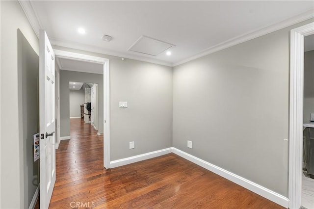 unfurnished room with attic access, wood-type flooring, crown molding, and baseboards