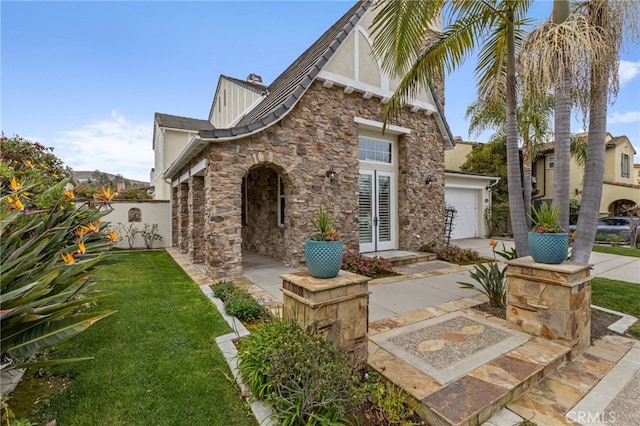 tudor house with a garage, a front yard, stone siding, and driveway