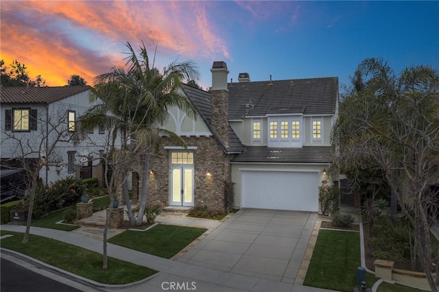 view of front of home with driveway, a garage, a chimney, a tiled roof, and stucco siding